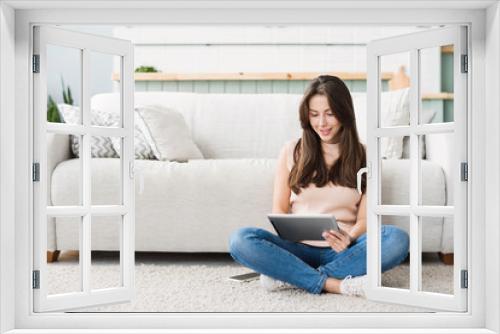 Beautiful  young woman with digital tablet relaxing at home. Happy smiling girl sitting in living room using tablet pc. Resting, relaxation, technology concept