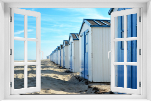 Fototapeta Naklejka Na Ścianę Okno 3D - Row of white and blue beach huts on the beach of island Texel in the Netherlands with blue sky on sunny summer day, selective focus with focus on right hut and copy space to the left