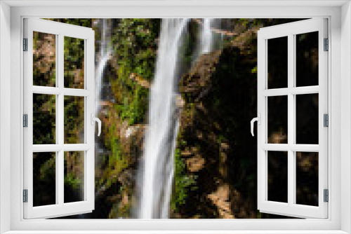 Fototapeta Naklejka Na Ścianę Okno 3D - View of a high waterfall with sunlight and surrounded by rainforest