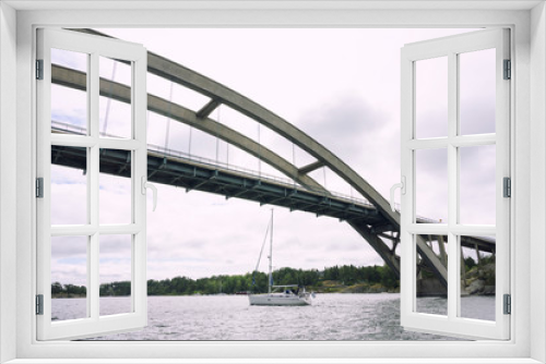 Fototapeta Naklejka Na Ścianę Okno 3D - Sailboat passing under the big bridge on the sea in Sweden with white clouds sky