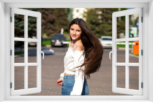 Young beautiful brunette woman in jeans and white blouse walking in summer street