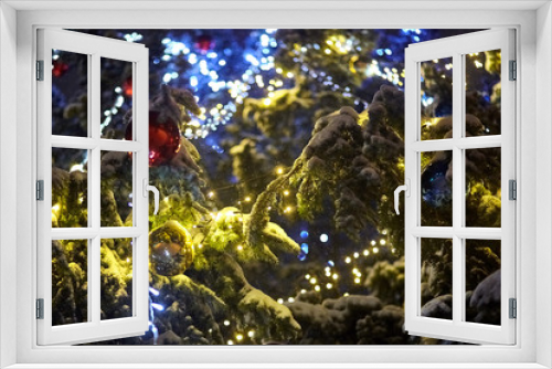 Fototapeta Naklejka Na Ścianę Okno 3D - Light garland and balls on Christmas tree. Winter time, light lamp decor. Electric night holiday illumination. Yellow and blue glowing bulbs on natural spruce branches covered snow