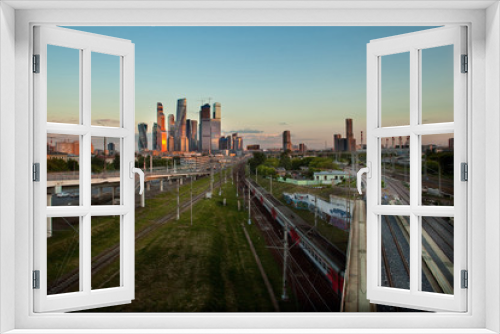 Fototapeta Naklejka Na Ścianę Okno 3D - Moscow City, a district of skyscrapers, Moscow, Russia, the sunset is reflected in the buildings, in the foreground - the railway, train, road factory pipes and residential buildings in the distance