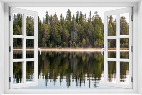 Fototapeta Naklejka Na Ścianę Okno 3D - Autumn with mirrored pine forest and misty Northern lake. Fog rises above the water at dawn. Finland, Scandinavia