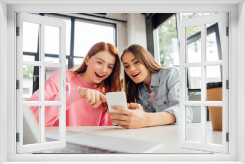 two excited girls smiling while using smartphone in school