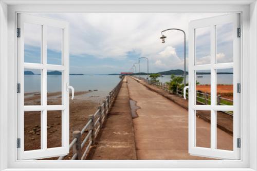 Fototapeta Naklejka Na Ścianę Okno 3D - Long pier at Koh Phangan island, Thailand, during low tide with clouds, boats, and mountains on the background.
