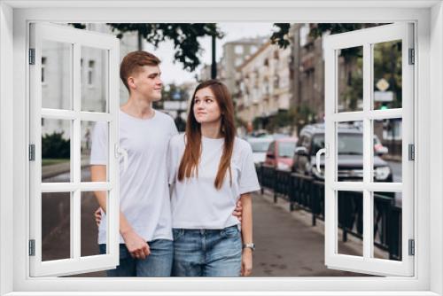 young couple walks the streets of the city and hold hands. guy and girl in white t-shirts and jeans outdoors. Teenagers walk in the autumn city. Happy young couple.