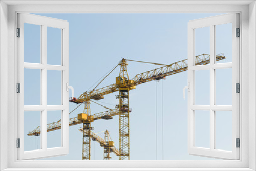 A yellow high-rise building crane against a blue sky builds multi-storey apartment buildings using modern technologies of metal, concrete and brick according to an architectural project