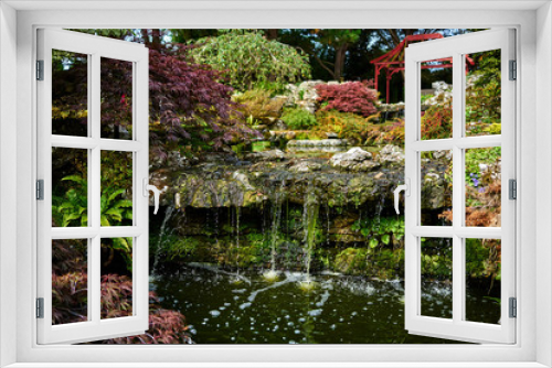 Fototapeta Naklejka Na Ścianę Okno 3D - Waterfall in a beautiful Japanese garden with the outline of a pagoda in the background