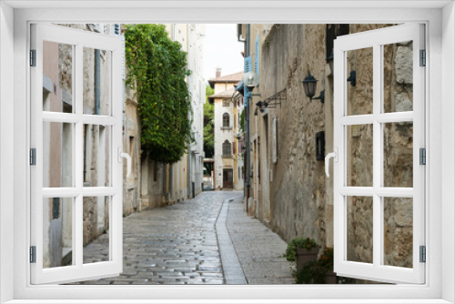 Fototapeta Naklejka Na Ścianę Okno 3D - A deserted narrow street in an ancient city. The building is located opposite each other, between them is a narrow path lined with white stone. Porec, Croatia.