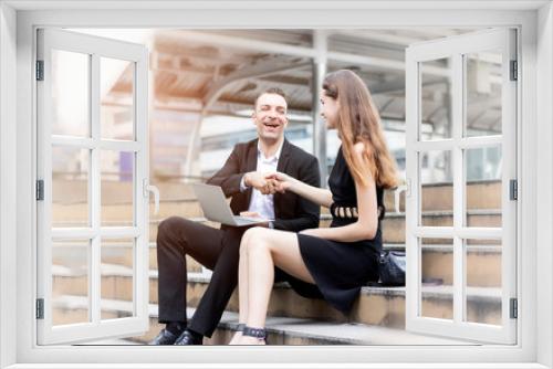 Successful business concept: Two happy young business people shaking hands while sitting in front of their office after working time.