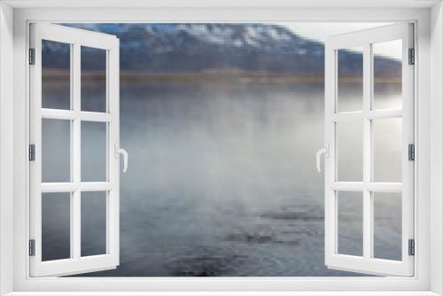 Fototapeta Naklejka Na Ścianę Okno 3D - Steam Rises off of Hot Springs in a Lake in Iceland with Snowy Mountains in the Background