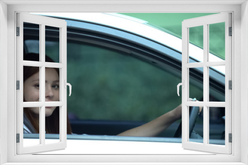 Girl sitting on driver seat in car smiling at camera, learner under instruction