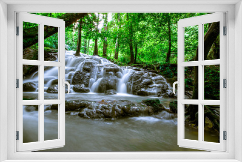 Fototapeta Naklejka Na Ścianę Okno 3D - The natural background of the water flowing through rocks, natural waterfalls, blur of flowing water surrounded by various plants, the integrity of the ecosystem.