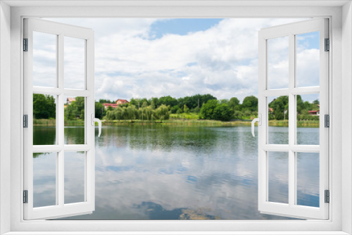 Fototapeta Naklejka Na Ścianę Okno 3D - calm lake with green vegetation and houses in the background