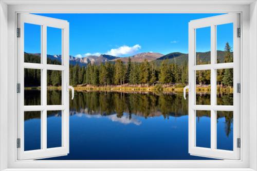 Fototapeta Naklejka Na Ścianę Okno 3D - Breathtaking mountain lake with tall pine trees reflecting in the water with mountain peaks in the background with clear blue sky with puffy white clouds