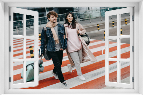 Young modern couple walking on crosswalk. Guy hold hand on suitcase. Attractive brunette walk besides man. Going to airport. Travel abroad.