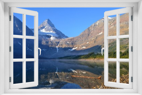 Fototapeta Naklejka Na Ścianę Okno 3D - Cold sunny morning in Assiniboine Provincial Park. Lake in front with rolling fog, Mount Assiniboine covered with snow in towering over whole scenery.