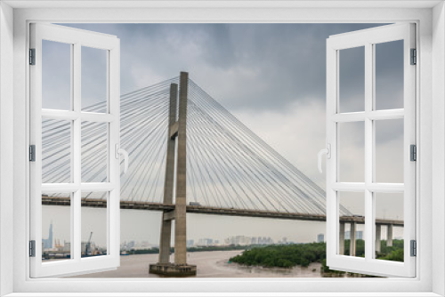 Fototapeta Naklejka Na Ścianę Okno 3D - Ho Chi Minh City, Vietnam - March 12, 2019: Long Tau and song Sai Gon rivers meeting point. Landscape with  H-shaped pylon of Phu My suspension bridge in center under gray cloudscape. Brown water.