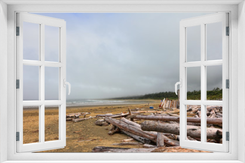 Fototapeta Naklejka Na Ścianę Okno 3D - The coast of the Pacific Ocean after the storm in the foggy morning. Logs and driftwood on the Tofino Long Beach ( year-round surfing )Vancouver Island. British Columbia, Canada