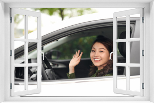 Hello! Beautiful young cheerful woman looking at camera with smile and waving while sitting in her car