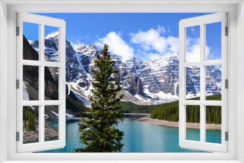 Fototapeta Naklejka Na Ścianę Okno 3D - This pristine Moraine Lake overlooks the icy rocky mountains and pine forest. The light breeze gently ripples the turquoise water towards the rocky edge on this partially cloudy day.