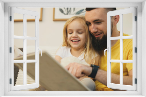 Portrait of a lovely little blonde girl laughing of how her father is reading a book. Happy father and daughter laughing while reading.