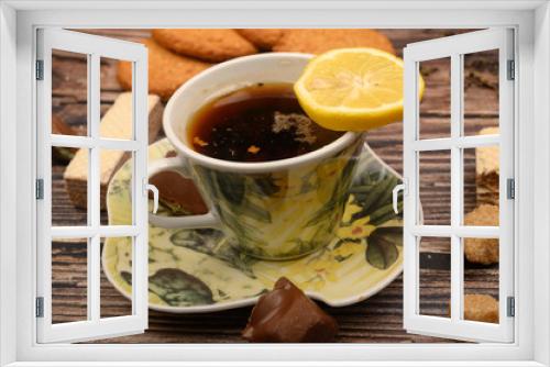 Fototapeta Naklejka Na Ścianę Okno 3D - A Cup of black tea, tea leaves, pieces of brown sugar, oatmeal cookies, waffles, pieces of chocolate, lemon on a wooden background. Close up.