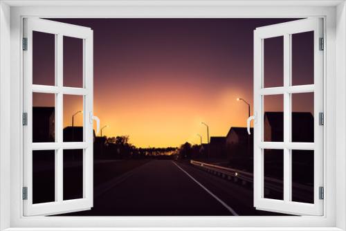 Fototapeta Naklejka Na Ścianę Okno 3D - Silhouettes of houses by a road during pinkish sunset