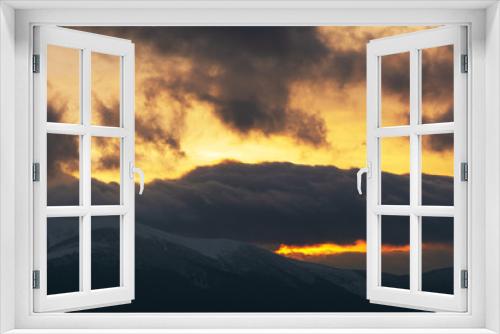 Fototapeta Naklejka Na Ścianę Okno 3D - Evening dramatic sky with colorful burning clouds against the backdrop of mountain houses in winter