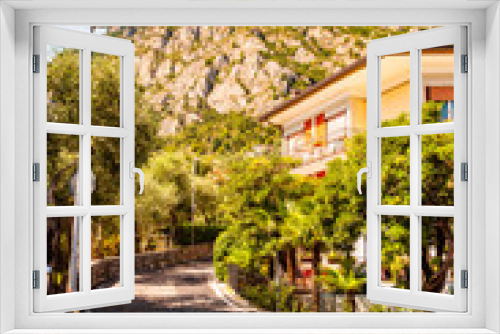Fototapeta Naklejka Na Ścianę Okno 3D - Cozy city street of Limone Sul Garda city with apartments, hotels and small businesses with high dolomite mountains on the background. Lombardy, Italy
