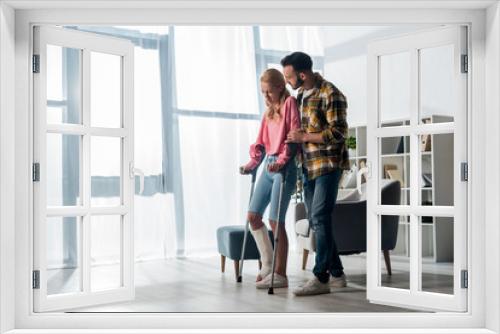 bearded man looking at injured woman holding crutches at home