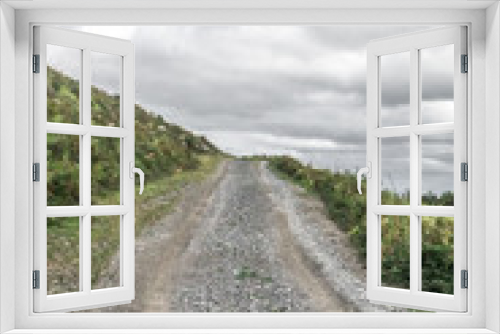 Fototapeta Naklejka Na Ścianę Okno 3D - The road goes into the distance. Winding path. Green tourism. Hiking in the nature. Camino de Santiago. Walk among the fields and trees. Road up to the sky. Country road with traces of cars.