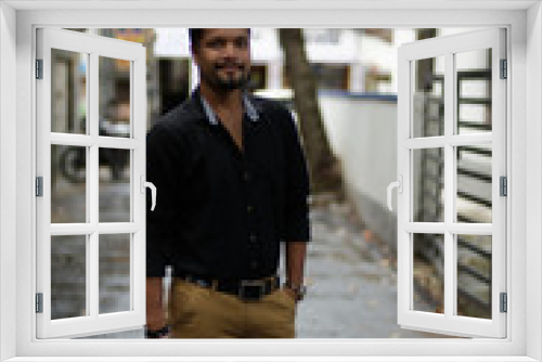 Portrait of a handsome brunette Indian bengali smart man in shirt and trousers standing in a drenched street in the morning of Durga Puja festival in urban background. Indian lifestyle.