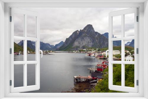 Fototapeta Naklejka Na Ścianę Okno 3D - The city of Reine in Lofoten/Norway. Long exposure shot with overcast scenery. The famous Mount Olstind and snow covered mountains in the background. Traveling and Norwegian concept.