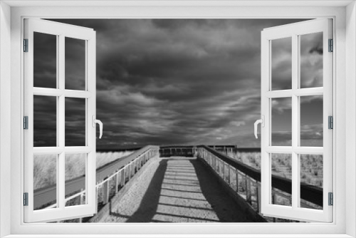 Fototapeta Naklejka Na Ścianę Okno 3D - a winter afternoon over a sandy wooden boardwalk leads to a cold beach over freshly planted grasses to protect against damage to sensitive sand dunes