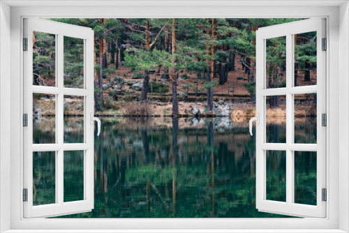 Fototapeta Naklejka Na Ścianę Okno 3D - Pine forest reflecting on the lake water in a mountainous area on a misty day