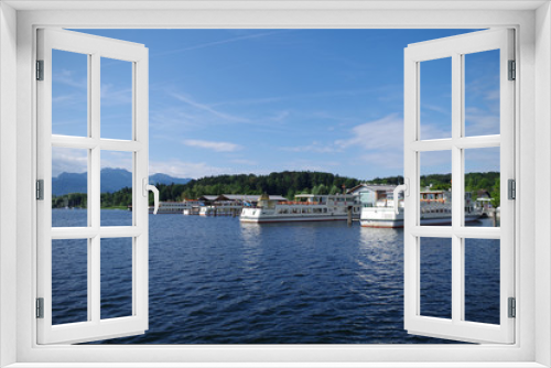Fototapeta Naklejka Na Ścianę Okno 3D - A view on the Chiemsee lake (Bavaria, Germany). There is a harbor with many passenger ships (ferries), as well as forested islands. The sky is very blue, there are scattered clouds.
