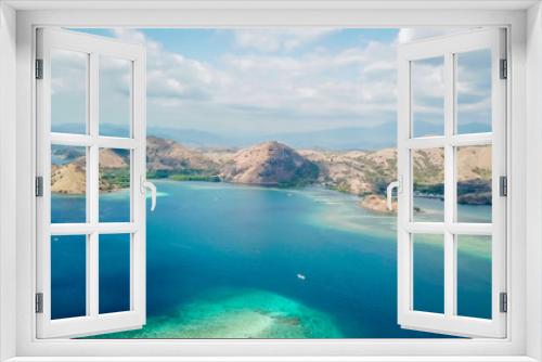 Fototapeta Naklejka Na Ścianę Okno 3D - A drone shot of a paradise island with some boats anchored around in Komodo National Park, Flores, Indonesia. Brownish island turns into white sand beach and further into turquoise and navy sea.