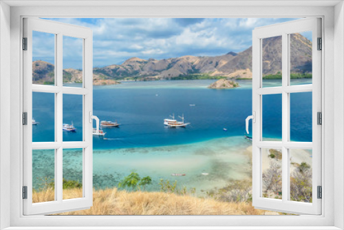 Fototapeta Naklejka Na Ścianę Okno 3D - View from top of a cliff on Kelor Island, Komodo, Indonesia. Island is surrounded with white sand beaches and turquoise water. There is another island in the back.There are boats anchored to a shore.