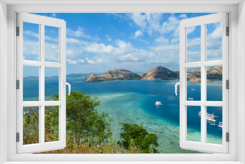 Fototapeta Naklejka Na Ścianę Okno 3D - View from top of a cliff on Kelor Island, Komodo, Indonesia. Island is surrounded with white sand beaches and turquoise water. There is another island in the back.There are boats anchored to a shore.
