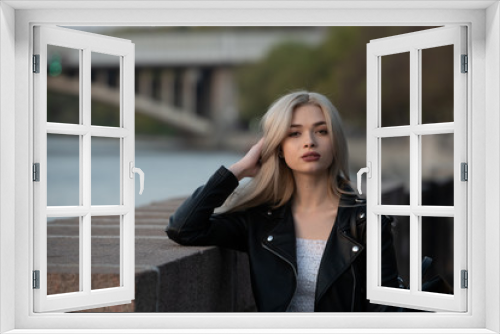 Young fashion blond woman in leather jacket with handbag on city street