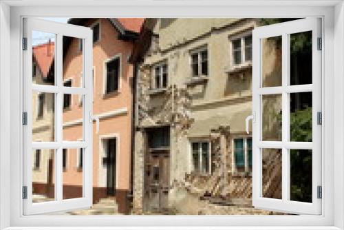 Fototapeta Naklejka Na Ścianę Okno 3D - Row of renovated attached old suburban family houses with one abandoned ruin at the end of street with dilapidated cracked walls and cracked wooden doors surrounded with paved road and tall trees