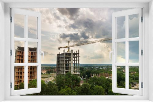 Fototapeta Naklejka Na Ścianę Okno 3D - Aerial view of tower lifting crane and concrete frame of tall apartment residential buildings under construction in a city. Urban development and real estate growth concept.