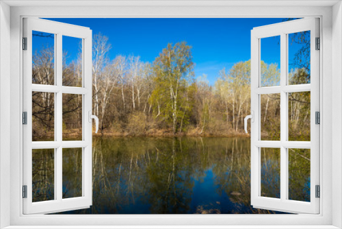 Fototapeta Naklejka Na Ścianę Okno 3D - Spring landscape - forest lake in early spring with trees around it, reflecting in blue water on a bright sunny day