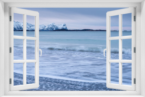 Fototapeta Naklejka Na Ścianę Okno 3D - Arctic landscape with long exposure Waves in foreground rolling to coast and snowy mountains in background on a cloudy winter day, Skaland, Senja, Norway