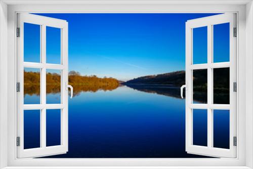 Fototapeta Naklejka Na Ścianę Okno 3D - autumn day, clear bright blue sky reflected in the river, one bank of the river is in shadow, the other is illuminated by the sun, autumn