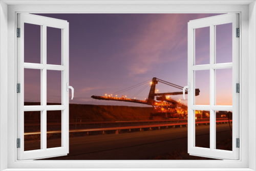 Fototapeta Naklejka Na Ścianę Okno 3D - Large mining industry equipment reclaimer machine, conveyor belts moving raw copper, silver, gold, from train load out stockyard to ship load out areas ready to export with sunset at the background 