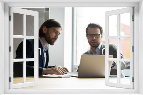 Two serious businessmen colleagues discussing project, looking at laptop screen