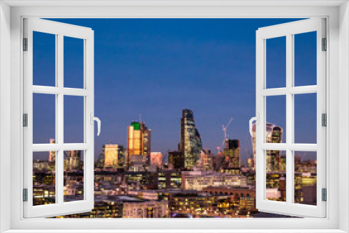 Fototapeta Naklejka Na Ścianę Okno 3D - City of London at dusk. An elevated view of the illuminated financial district skyline fronted by the River Thames riverside.